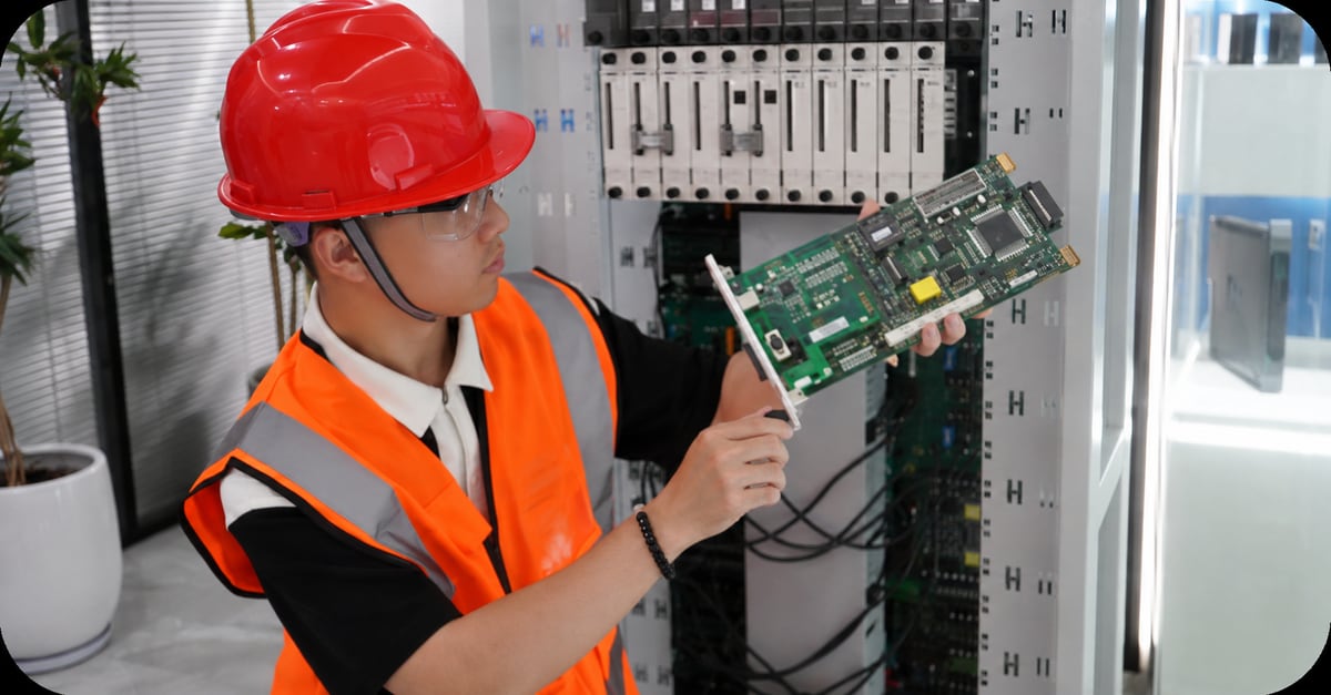 Technician holding a circuit board beside a control cabinet; original article photograph enhanced with AI